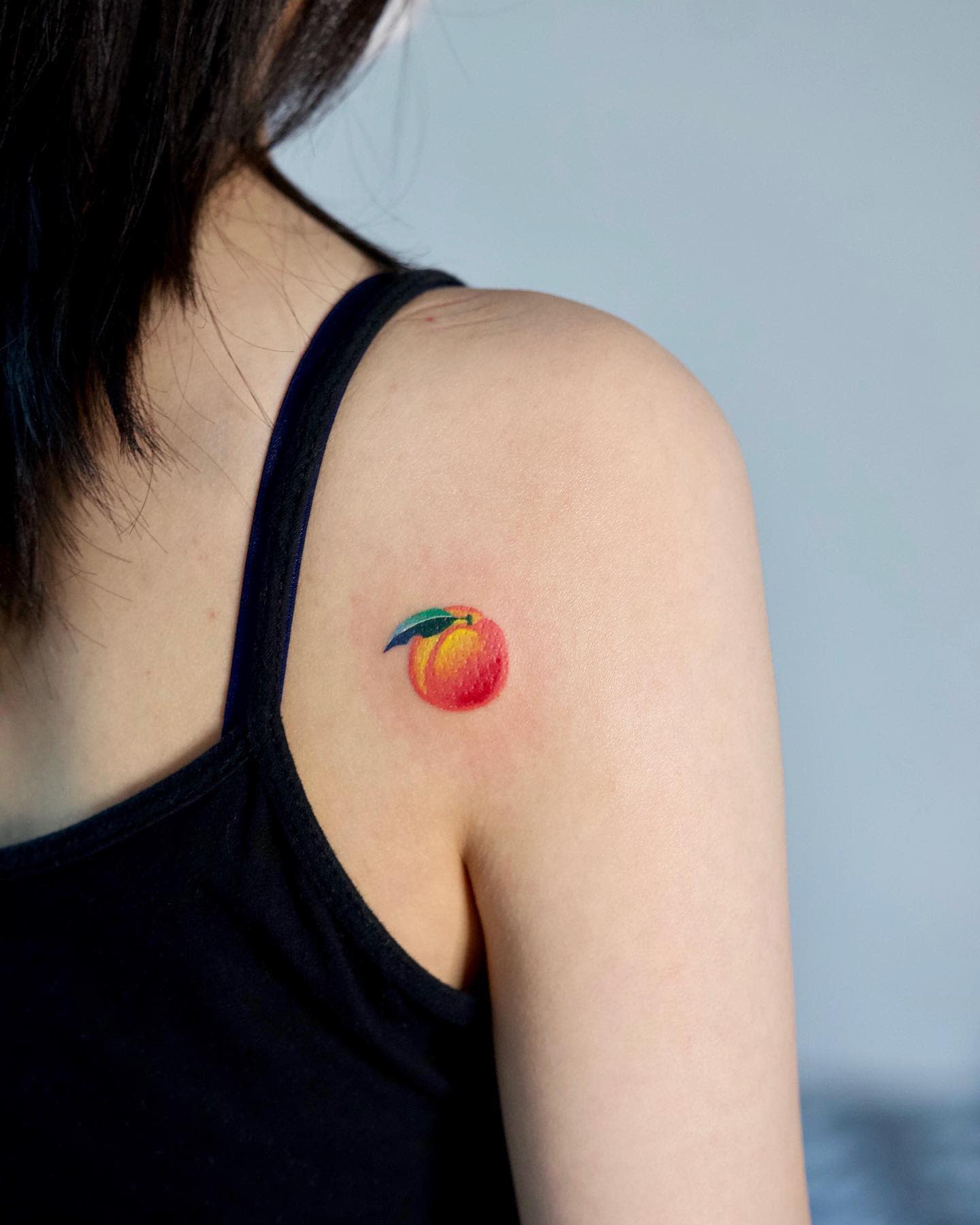 A small, colorful peach tattoo on a shoulder
